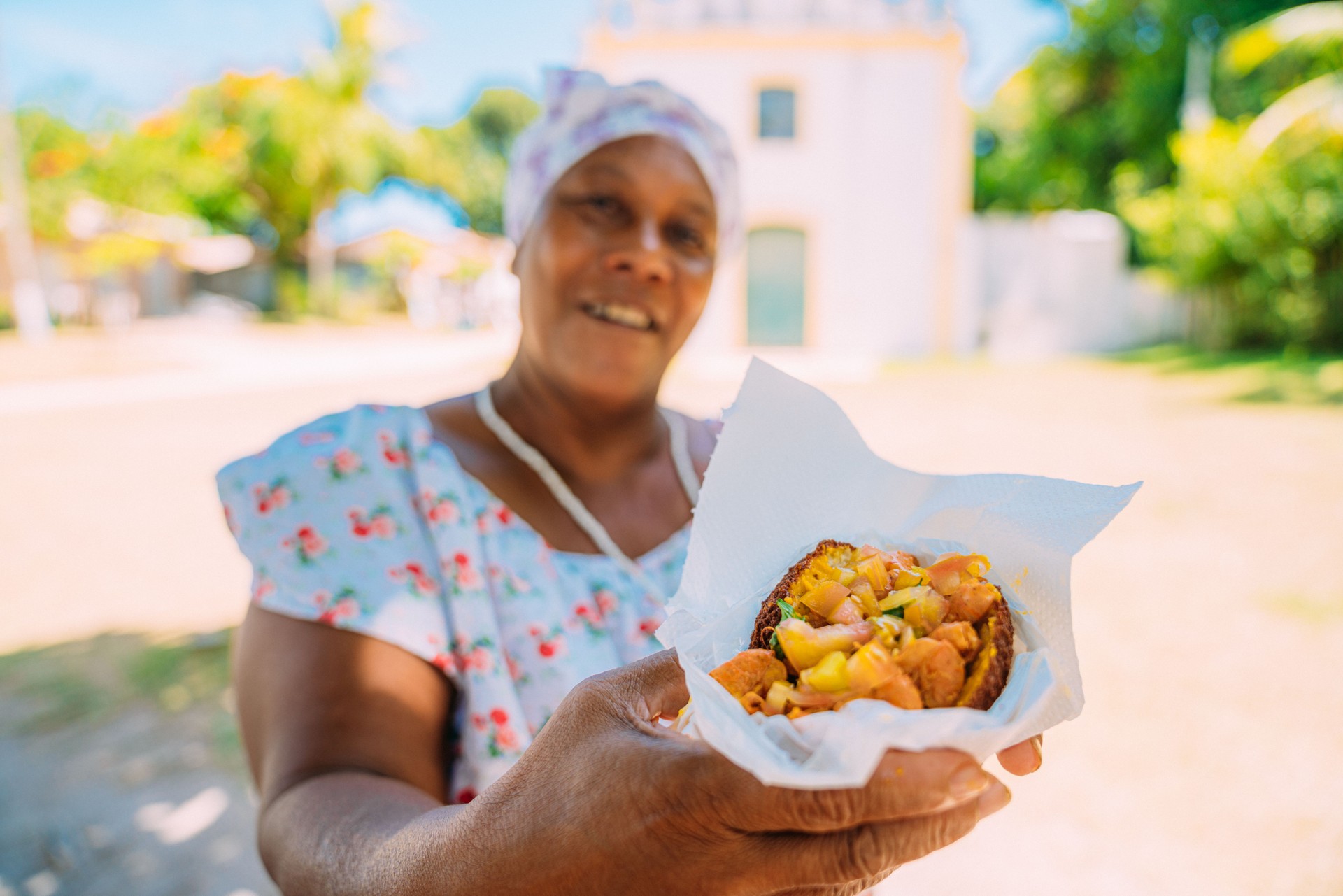 Happy Brazilian woman dressed in the traditional Bahian costume of the Umbanda religion, offering acarajé